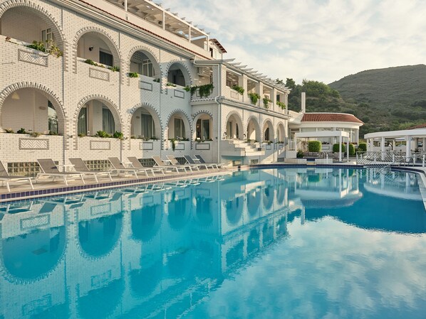 A large pool with clear blue water, surrounded by a white building with arched windows and balconies. - Meandros Boutique & Spa Hotel - Adults Only (Zakynthos)