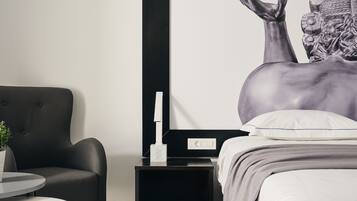Un dormitorio moderno con una mesita de noche negra, una mesita de cabecera blanca, una silla negra y una cama con almohada blanca.