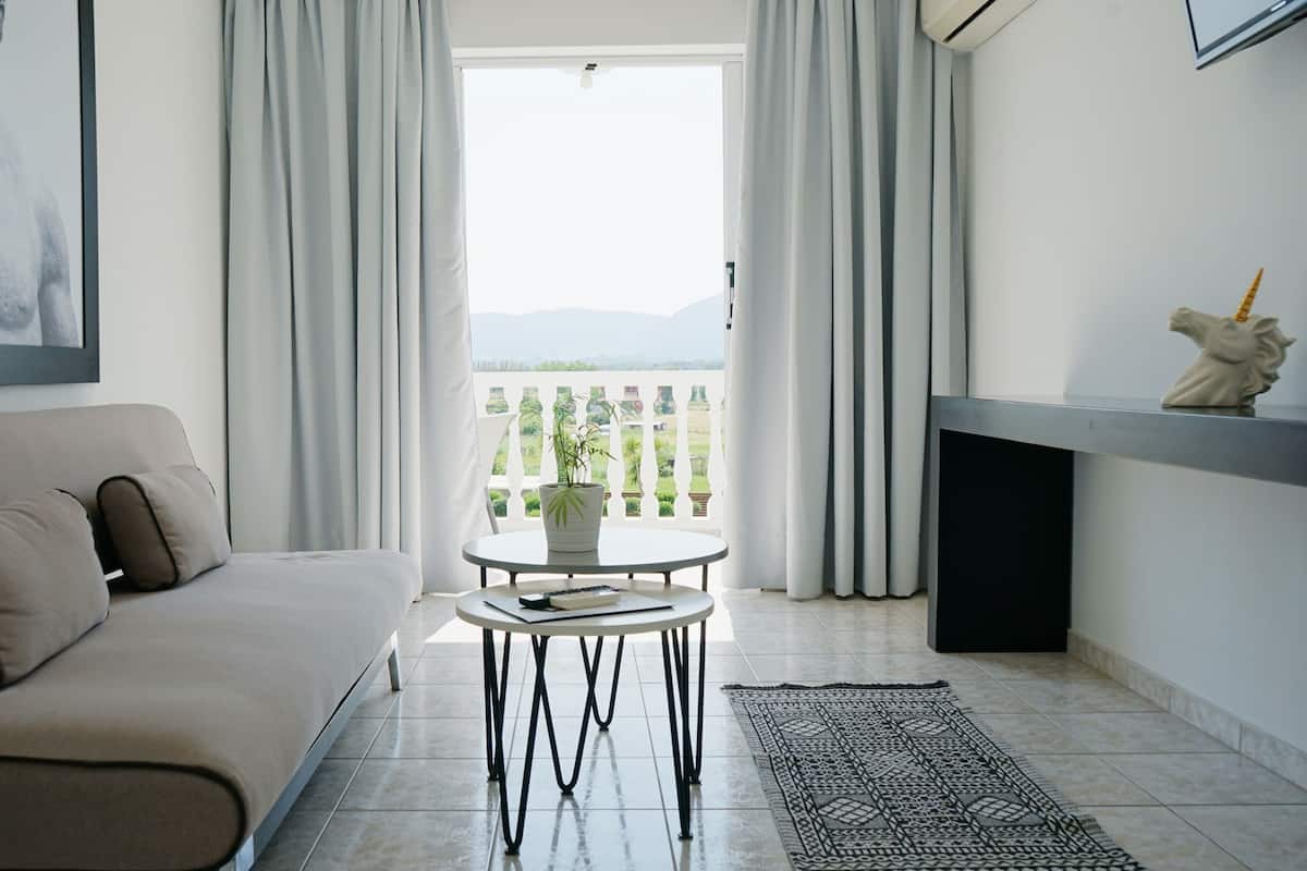 Una sala de estar moderna con un sofá, una pequeña mesa redonda con una planta y vistas a un balcón con cortinas.