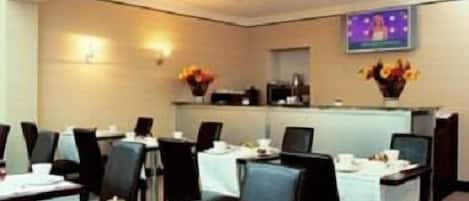Ein Essbereich eines Hotels mit gedeckten Tischen, Stühlen und einem Fernseher an der Wand.
