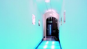 A hallway with a blue-lit floor, a door at the end, and a plant on the right.