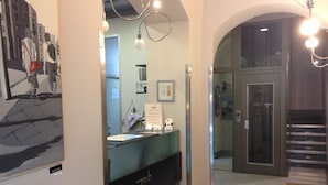 A hotel reception area with a reception desk, a framed picture on the wall, and a staircase leading to the upper floor.