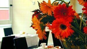 A dining area with tables set for tea service, featuring a vase of orange flowers.