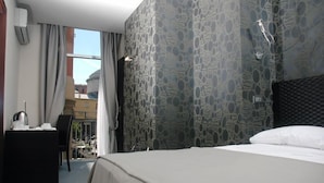 A hotel room with a bed, a desk with a chair, and a view of the outside.
