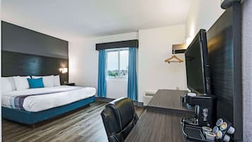 A hotel room with a bed, a desk with a coffee maker, a TV, and a window with curtains.