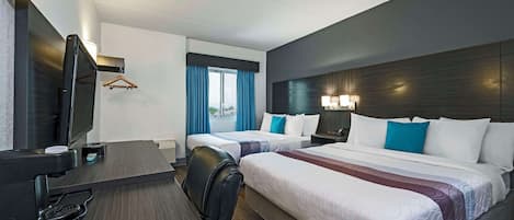 Ein Hotelzimmer mit zwei Betten, einem Schreibtisch mit Fernseher und einem Fenster mit Vorhängen.