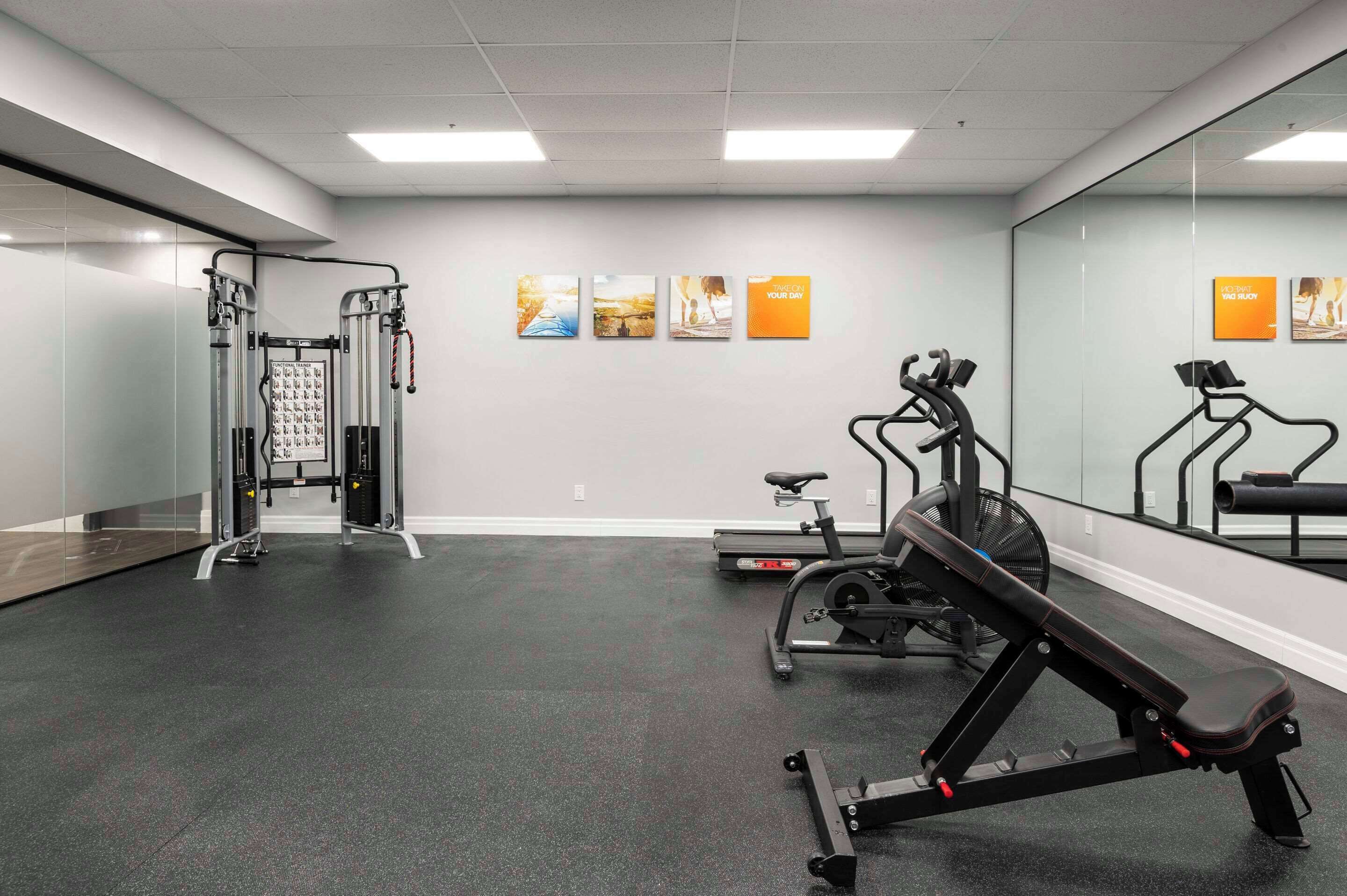 A gym with exercise equipment, a treadmill, and a mirrored wall.