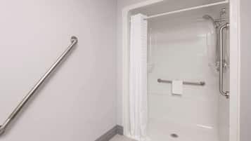 A modern bathroom with a walk-in shower, grab bars, and a white tiled floor.