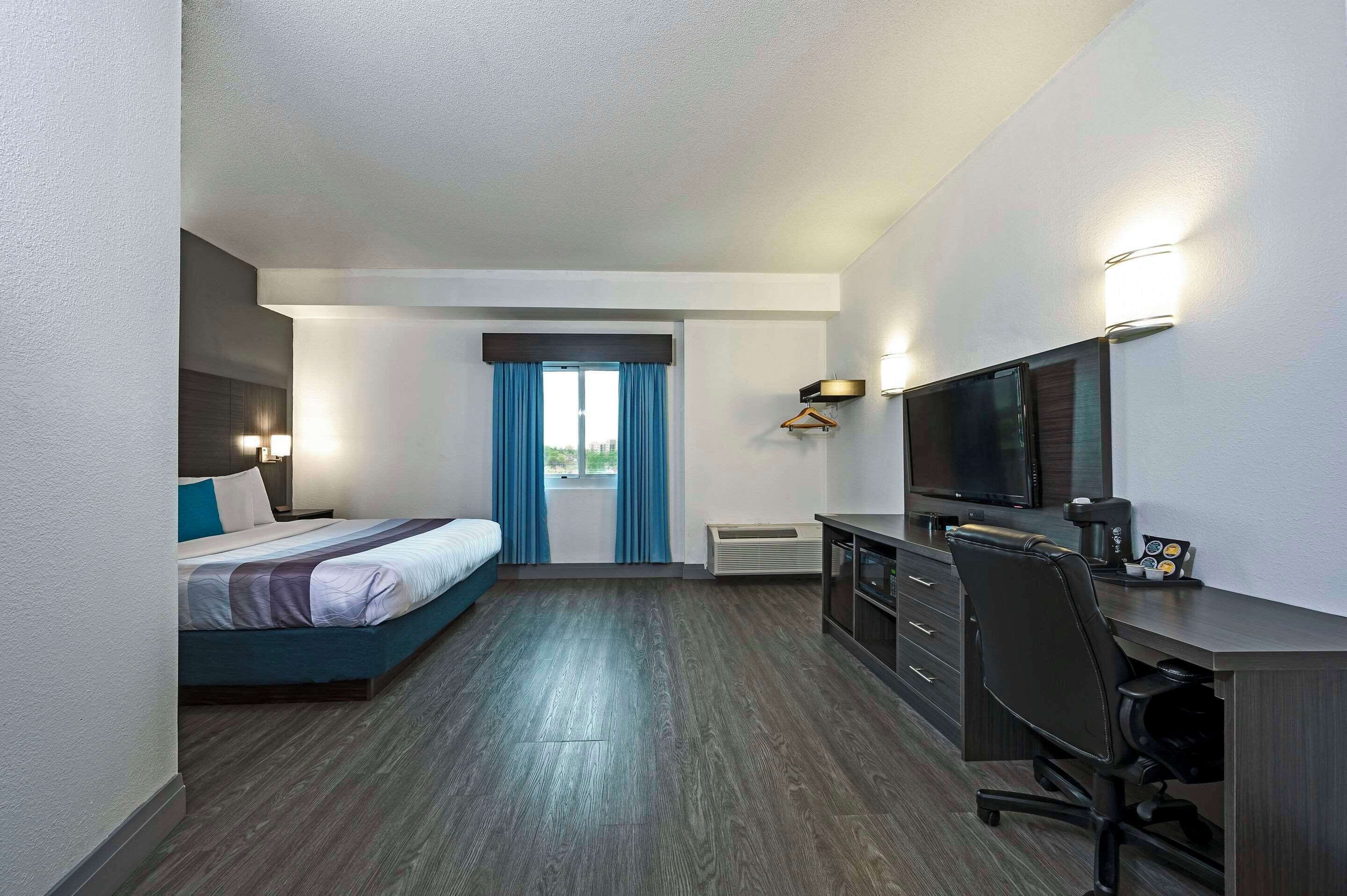 Habitación de hotel con cama, escritorio, silla, televisión y vistas a la ciudad por la ventana.