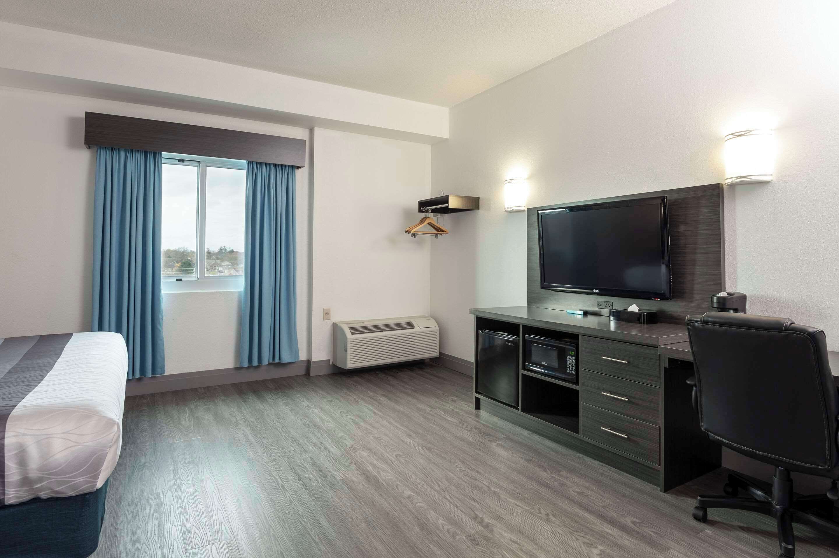 Ein Hotelzimmer mit einem Bett, einem Schreibtisch, einem Stuhl, einem Flachbildfernseher, einer Heizung und einem Fenster mit Vorhängen.