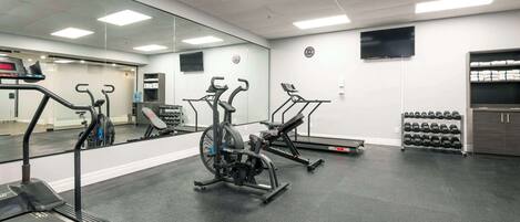 A gym with cardio machines, dumbbells, and a bench.