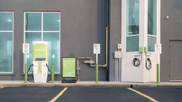 Un aparcamiento con estaciones de carga para vehículos eléctricos, un cartel de AmbuEnergy y un edificio con grandes ventanales.