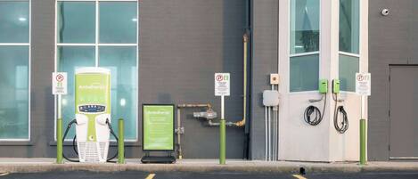 A parking area with electric vehicle charging stations, a sign for AmbuEnergy, and a building with large windows.