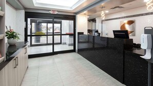 A modern reception area with a glass door entrance, a black reception desk, and a ceiling with recessed lighting.