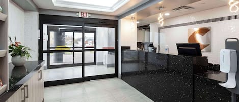 A modern reception area with a glass door entrance, a black reception desk, and a ceiling with recessed lighting.