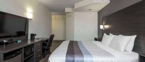 Una habitación de hotel con cama, escritorio con televisor, microondas y una silla.