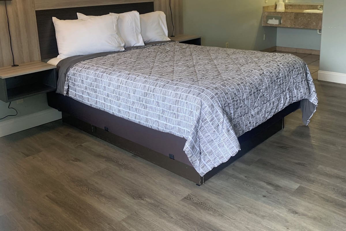 A bedroom with a large bed, two bedside tables, a nightstand, a wall-mounted lamp, and a bathroom visible in the background.