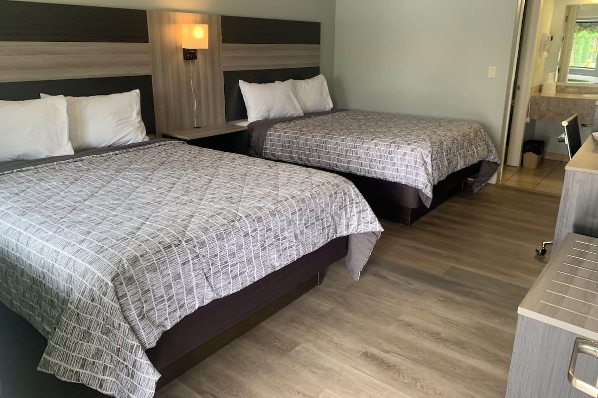 A hotel room with two beds, a nightstand, a wall-mounted lamp, and a wooden floor.
