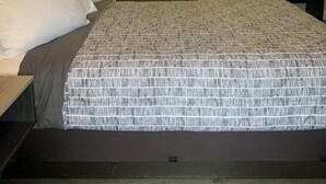 A hotel room with a large bed, a bedside table, a nightstand, a bathroom mirror, a vanity with a sink, and a wall-mounted mirror.
