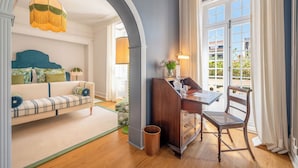 Een kamer met een bank, een bureau met stoel, een lamp en uitzicht door een raam.