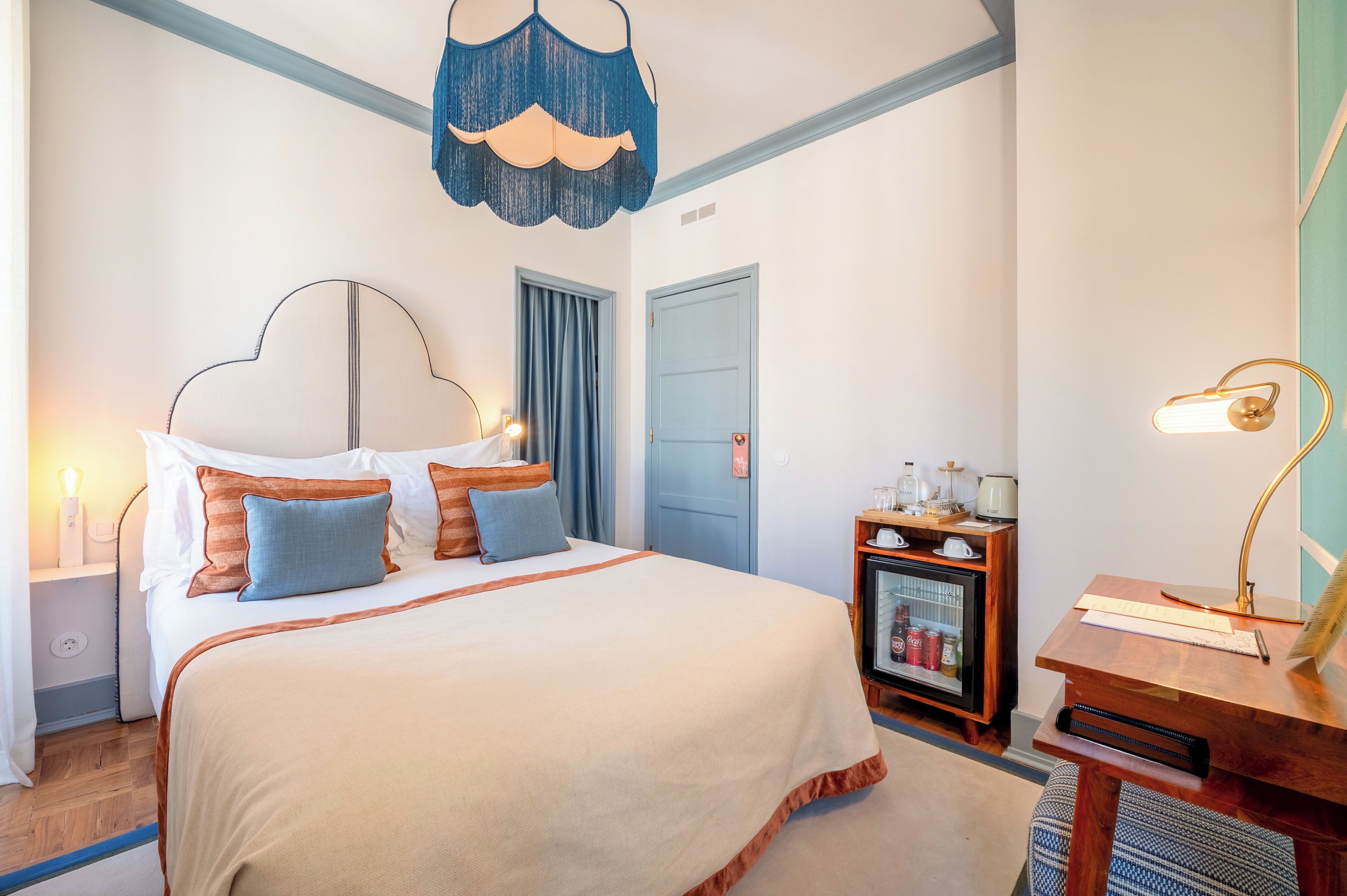 A neatly arranged bedroom with a bed, bedside tables, a desk, and a small cabinet.