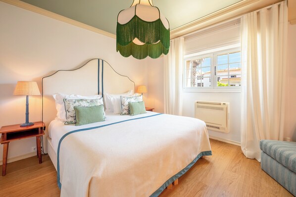 A neatly made bed with a white and blue bedspread, two green pillows, and a wooden nightstand with a lamp.