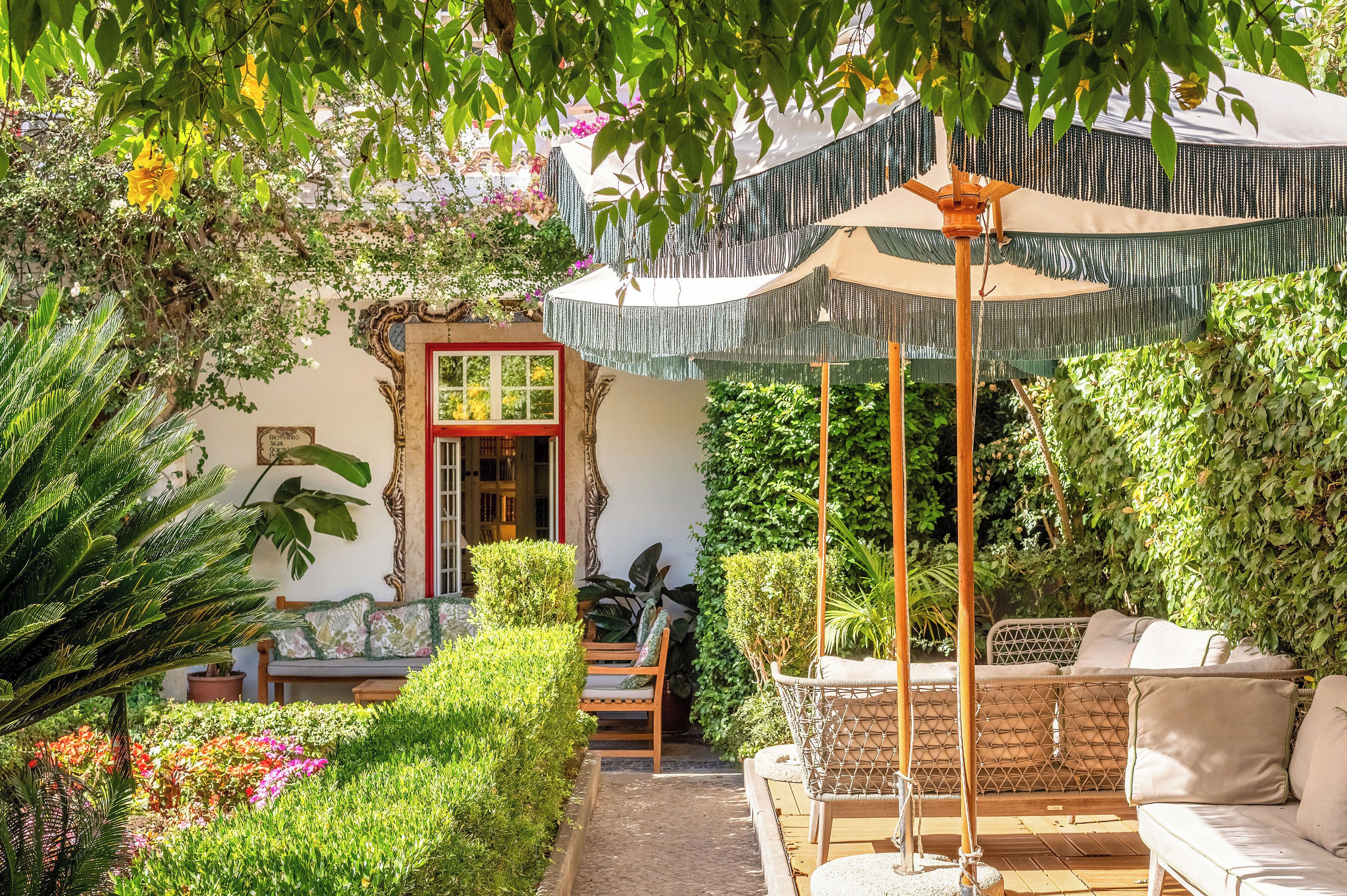 Ein Garten mit Sitzgelegenheit, einer kleinen Struktur mit roter Tür und einem Sonnensegel.