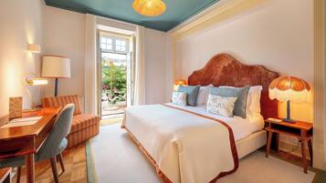 Quarto de hotel com uma cama grande, uma escrivaninha de madeira, uma cadeira e uma mesa com abajur.