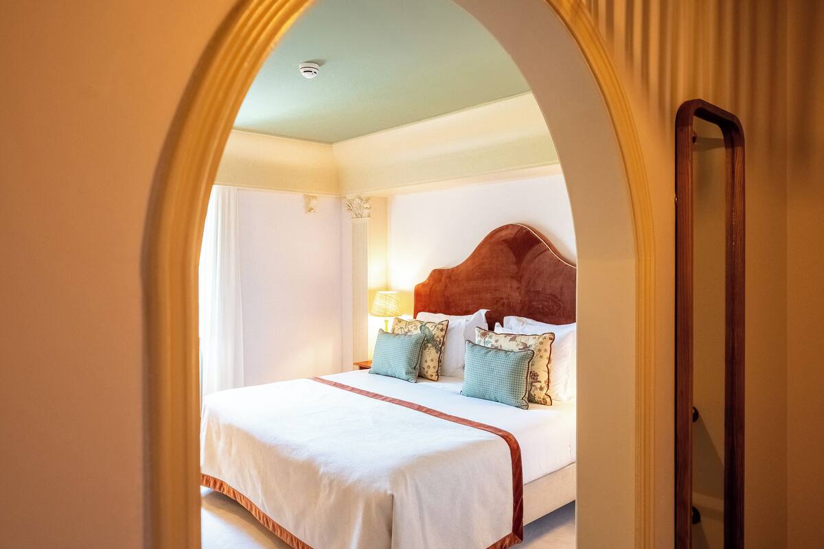 A hotel room with a large bed, a wooden headboard, and a nightstand with a lamp.