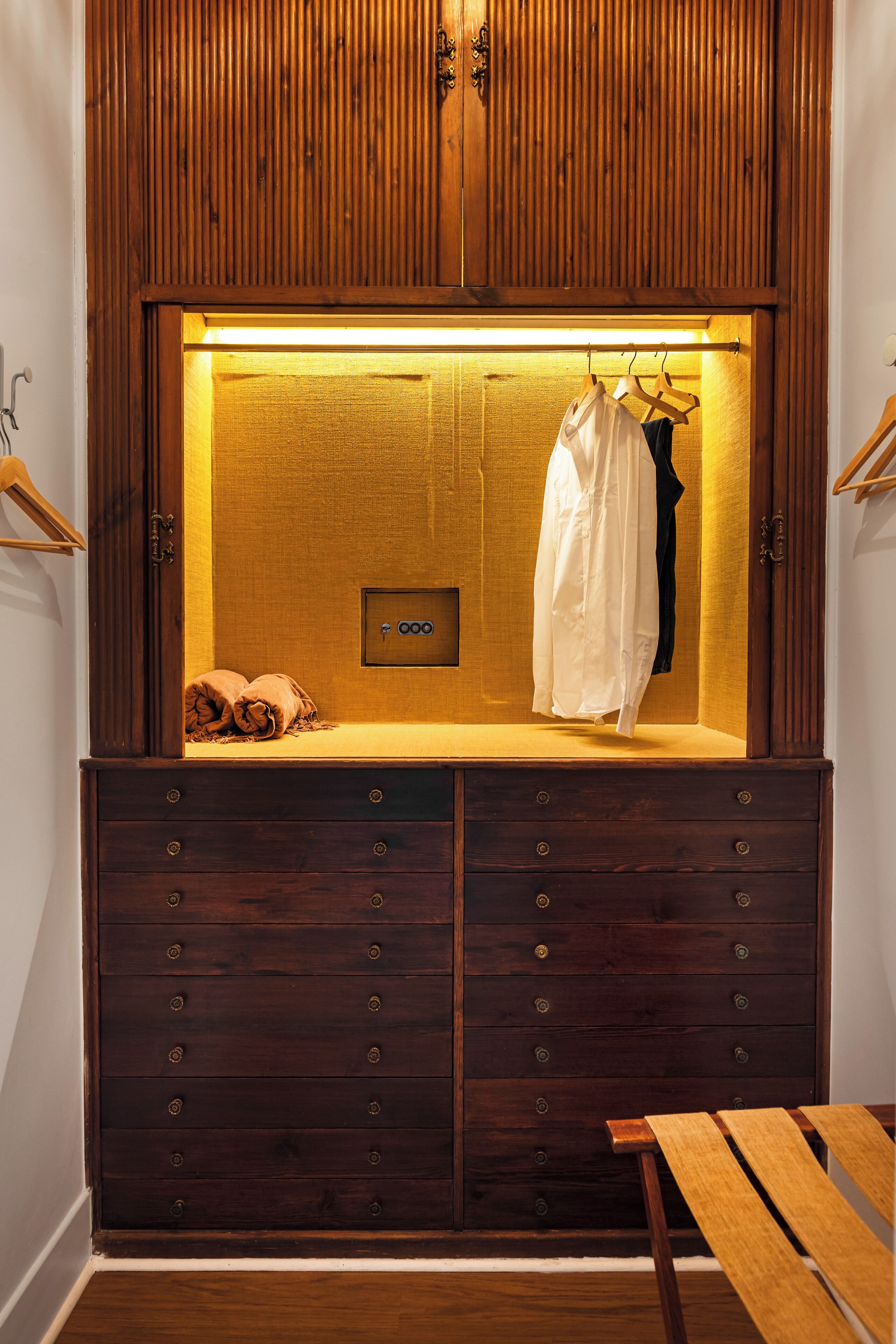 Une armoire en bois dotée d’un éclairage intégré, d’une tringle pour suspendre les vêtements et d’un banc.