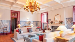 Een ruime woonkamer met een bank, fauteuils, een salontafel en een kroonluchter.