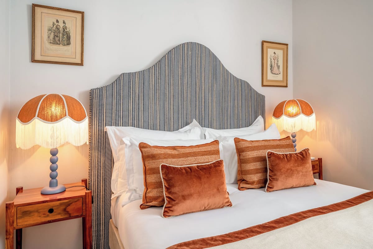 A neatly made bed with striped headboard, two bedside lamps, and three pillows.