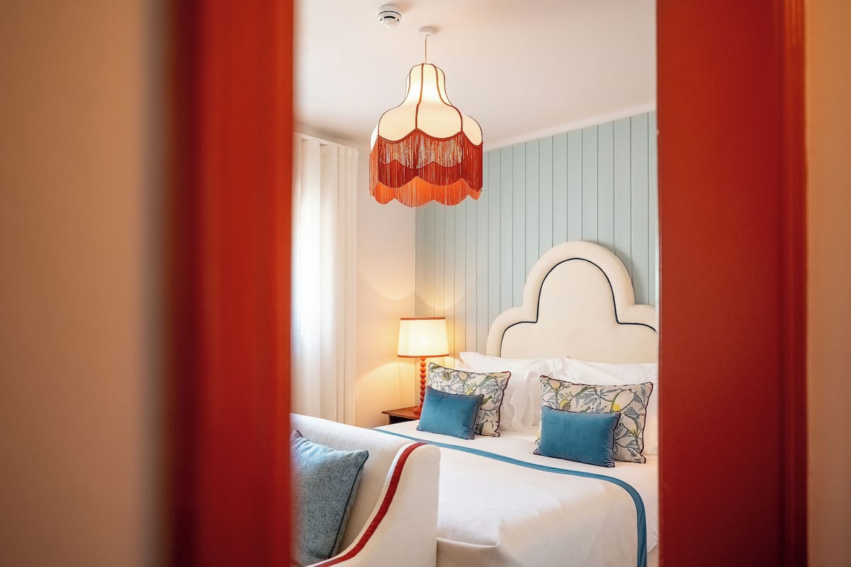 A hotel room with a bed, a nightstand, a lamp, and a hanging light fixture.