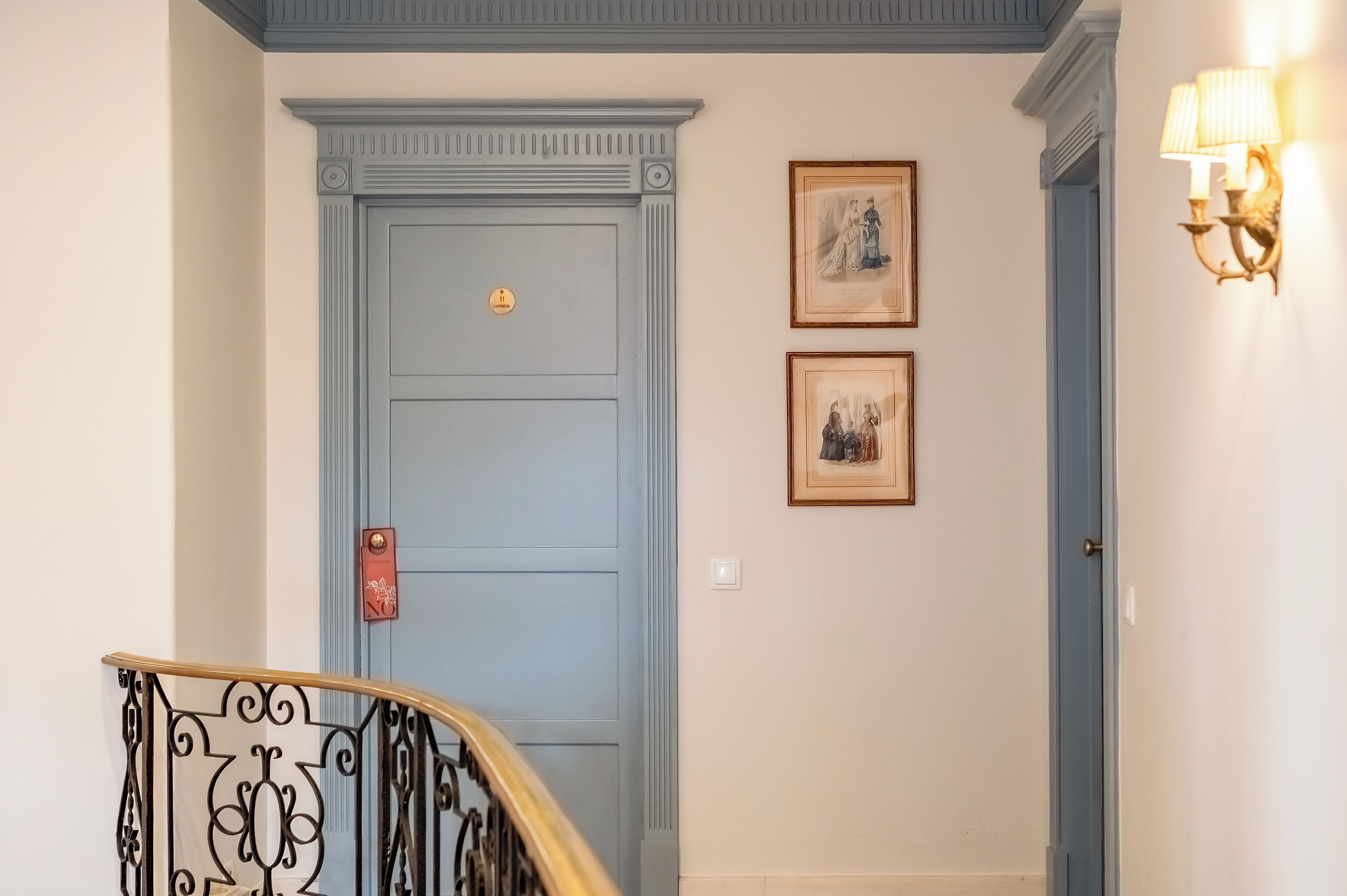 Una puerta azul con una placa dorada, un timbre rojo y dos cuadros en la pared.