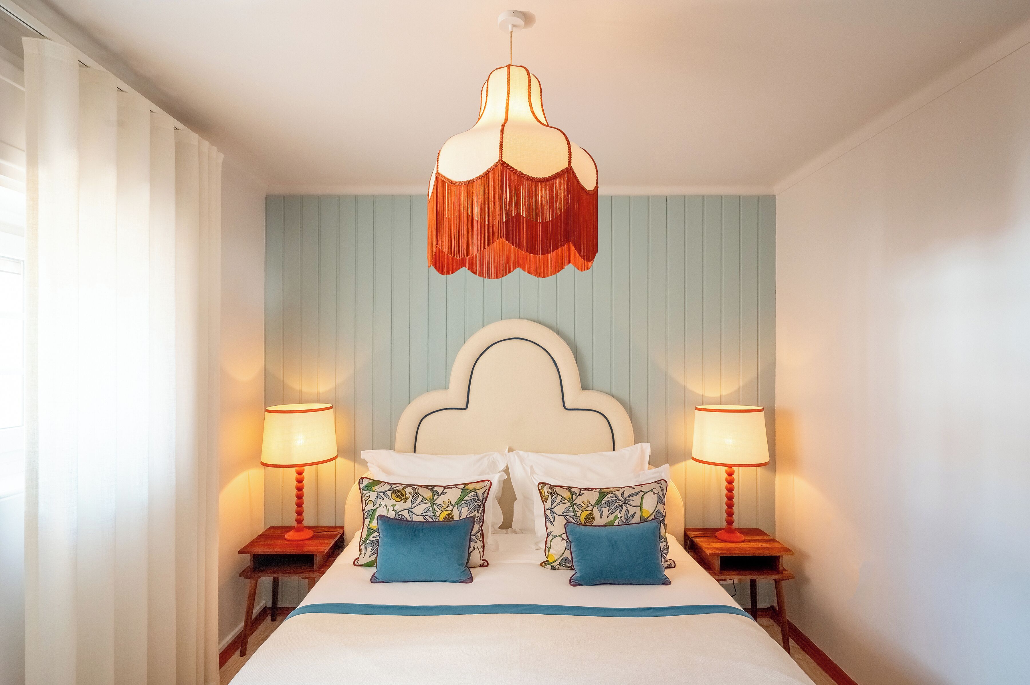 A bedroom with a large bed, two bedside tables with lamps, a decorative ceiling light, and a wall with vertical paneling.