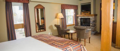 A hotel room with a large bed, a fireplace, a small table with chairs, and a television.