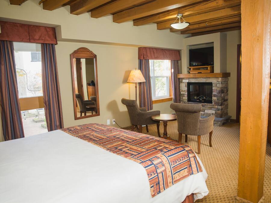 A hotel room with a large bed, a fireplace, a small table with chairs, and a television.