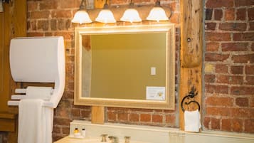 A bathroom with a brick wall, a wooden-framed mirror, a white sink, and a towel rack.