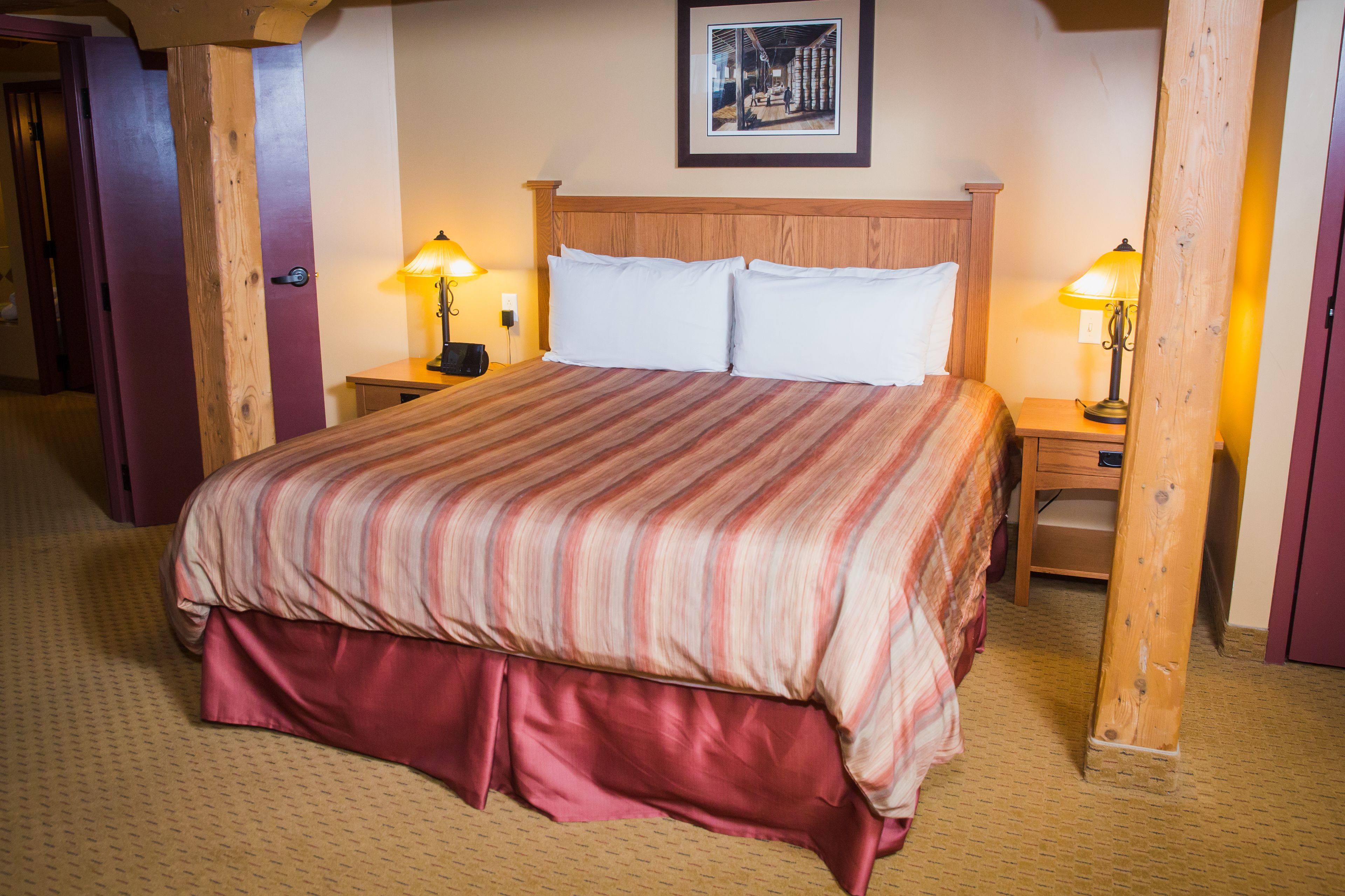 A hotel room with a large bed, two bedside tables with lamps, a wooden headboard, and a framed picture on the wall.