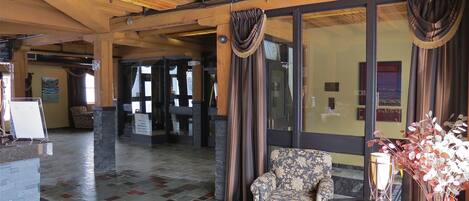 A lobby with a wooden ceiling, a patterned armchair, a vase with flowers, and a tiled floor.