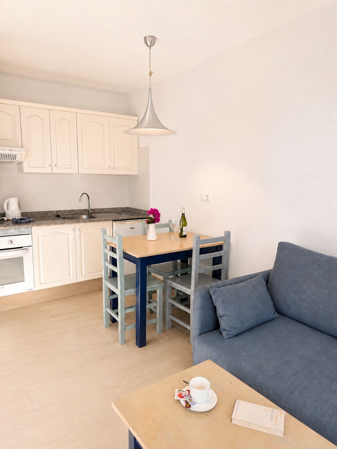 A modern kitchen with white cabinets, a dining table, and a blue sofa in a living area.