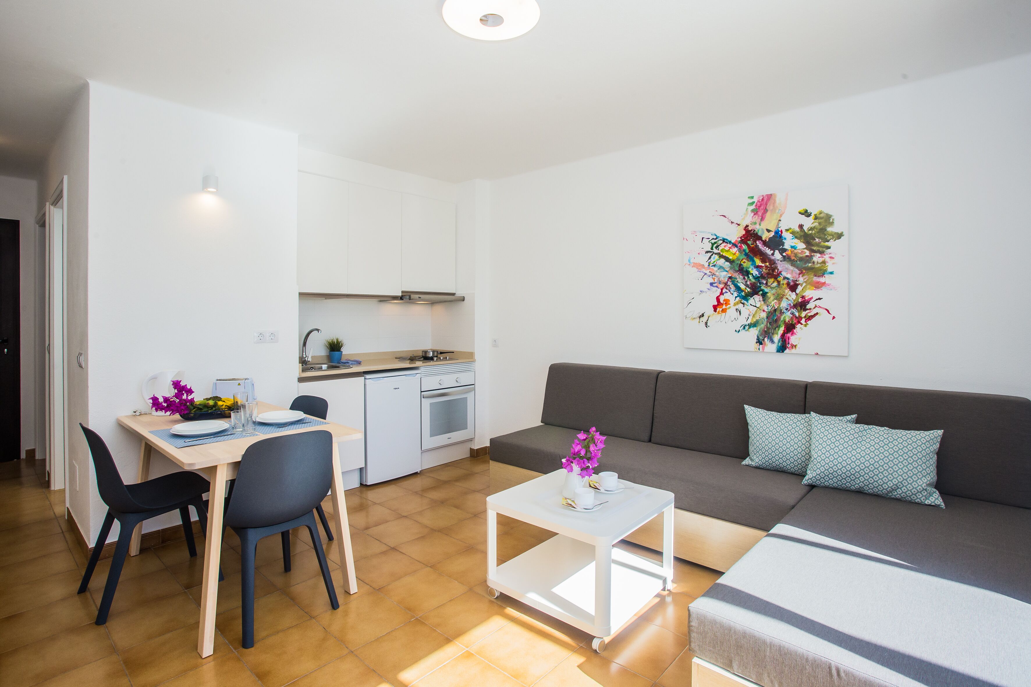 A modern apartment with a dining area, kitchenette, and a living room with a sofa and a painting.