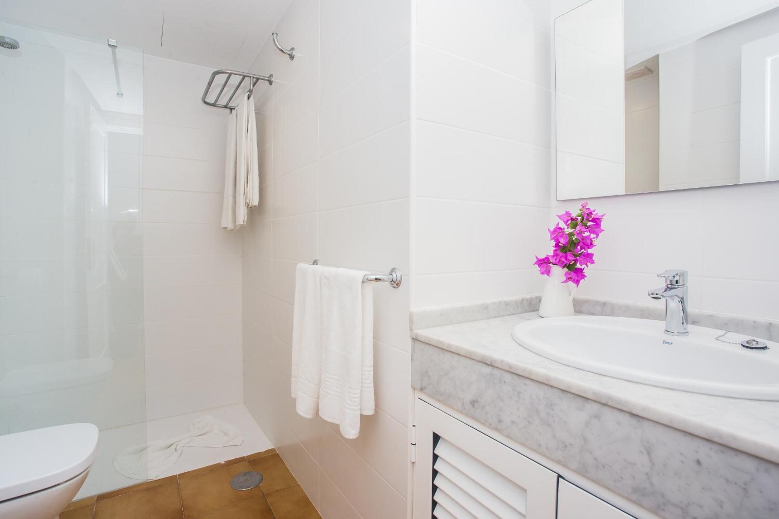 A modern bathroom with a glass shower enclosure, a white toilet, a marble sink, and a mirror above the sink.