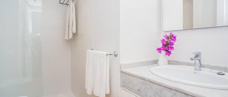 A modern bathroom with a glass shower enclosure, a white toilet, a marble sink, and a mirror above the sink.