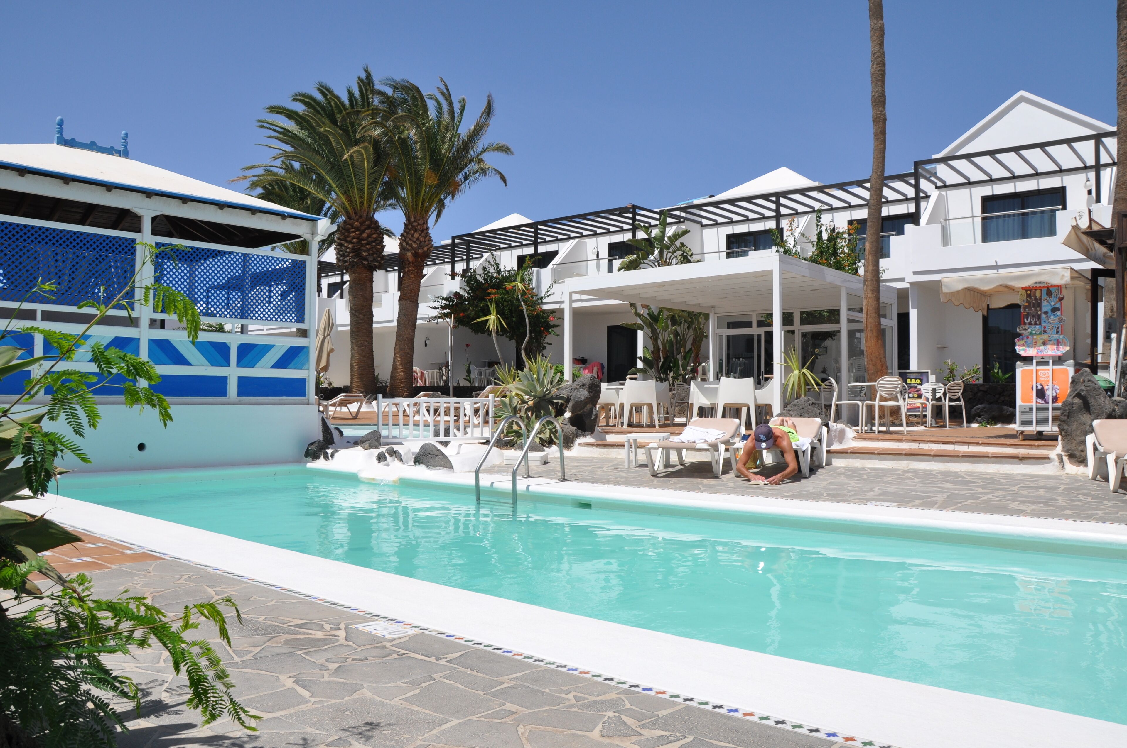 A pool area with lounge chairs, palm trees, and a covered seating area.