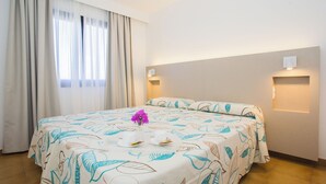Quarto de hotel com cama, cortinas, luminária na parede e uma janela.