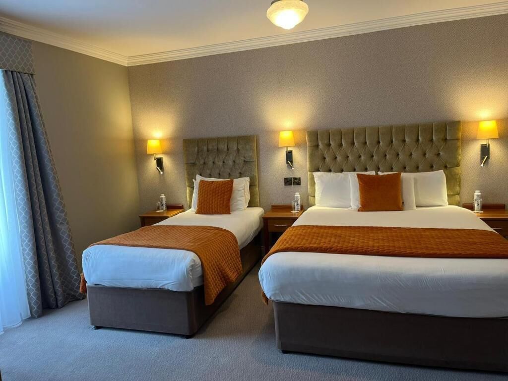 Habitación de hotel con dos camas, cada una con un cabecero capitonado, lámparas de noche y una paleta de colores neutros.