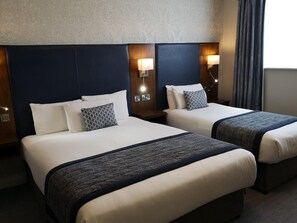 A hotel room with two beds, each with a headboard, bedside lamps, and a patterned throw blanket.