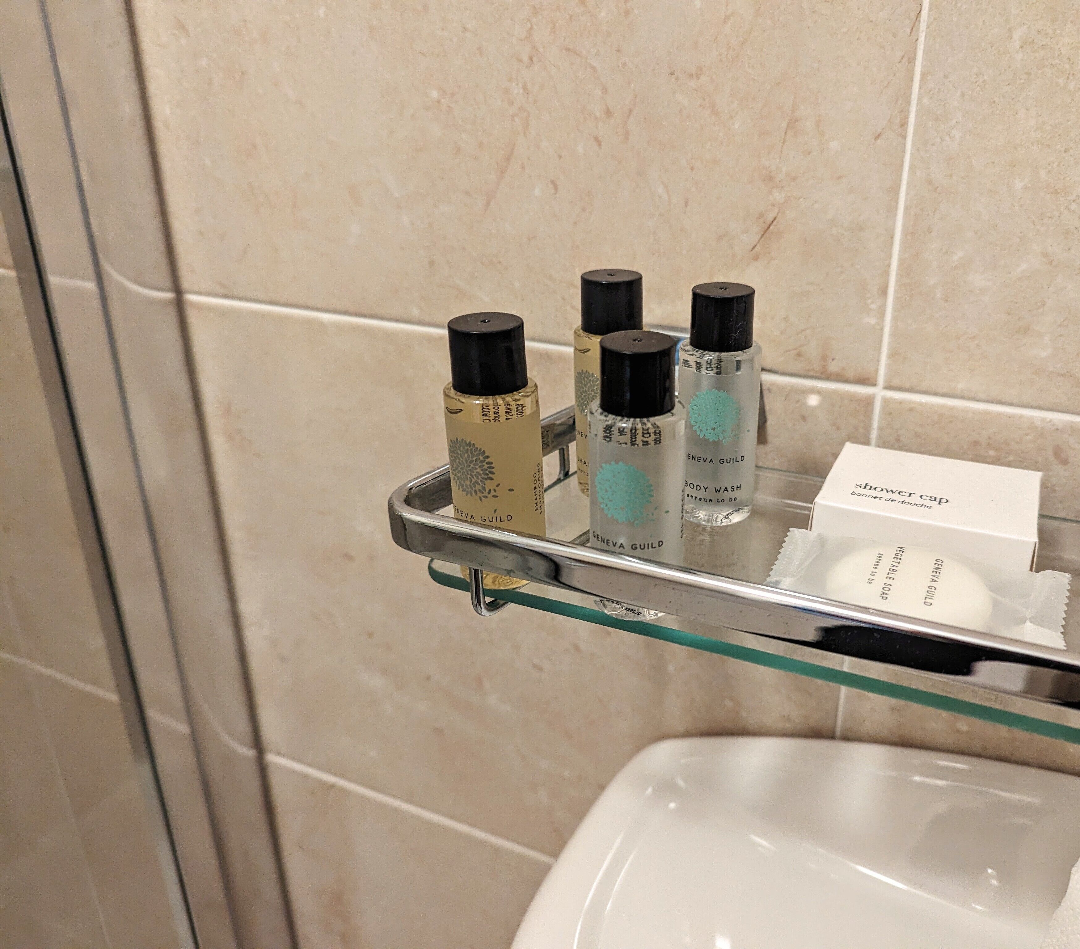 Un baño con repisas de vidrio que sostienen artículos de aseo personal y un gorro de ducha.