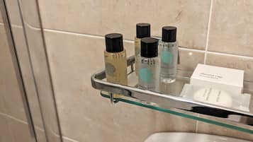 Un baño con repisas de vidrio que sostienen artículos de aseo personal y un gorro de ducha.